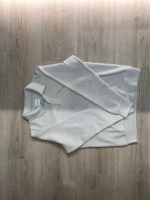 Beige sweatshirt med krage - Snygg beige sweatshirt med klassisk krage och knappslå framtill. Tröjan har långa ärmar och ribbade muddar vid ärmslut och nederkant. Perfekt för en avslappnad och stilren look.