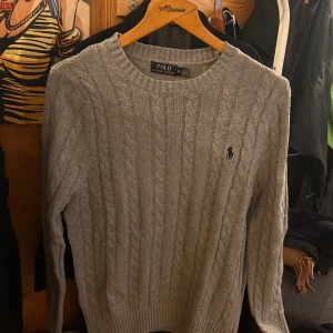 Grå kabelstickad tröja från Ralph Lauren - Säljer en stilren grå stickad tröja från Ralph Lauren med kabelstickat mönster. Storlek M och väldigt bra skick. (Inte mina bilder) pris är inte hugget i en sten