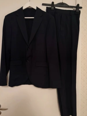 Mörkblå kostym med kavaj och byxor - En perfekt mörkblå tiger kostym i ett mycket bra skick i storlek 46. Byxorna är nedsydda men går självklart att sy upp igen. 