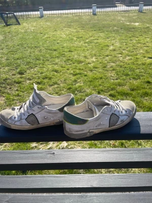 Philipe model - Säljer ett par vita låga sneakers med grå mockadetaljer och grönt parti vid hälen. Skorna har klassisk snörning och en stilren design som passar till det mesta. Ett snöre har typ knäckts lite men jag kan skicka med snöret i paketet. Pris kan diskuteras!