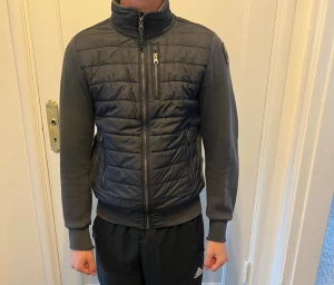 Svart pufferjacka från Parajumpers - Snygg svart pufferjacka från Parajumpers med quiltad front och släta ärmar. Jackan har hög krage, dragkedja framtill, bröstficka med dragkedja och två sidofickor. Märkespatch på vänster ärm. Perfekt för kalla dagar.