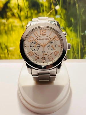 Michael Kors Chronograph Damklocka  - Stilren klocka från Michael Kors i silverfärgat metallarmband och boett. Urtavlan är vit med roséguldfärgade siffror och visare samt tre mindre urtavlor för extra funktioner. Perfekt accessoar för att lyfta din outfit. Nyligen servad med nytt batteri, säljes i befintligt skick enligt bilderna! Levereras i original MK box. 