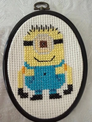 Broderad tavla med Minion-motiv - Handgjord broderad tavla med en Minion i blå overall, svart ram och vit bakgrund. Motivet är broderat med färgglada trådar i gult, blått, svart och brunt. Perfekt som dekoration till rummet eller som present till någon som gillar tecknade figurer.
