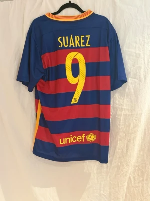 Barcelona 15-16 Suárez #9 - En Barcelona tröja  med Suárez och nummer 9 på ryggen. Tröjan är från säsongen efter Barcelona vann sin femte Champions leauge titel då  Suárez spelade mellan sina radarpartners Neymar och Messi. Bara att höra av sig vid frågor!