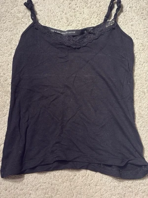 Svart spetslinnetopp - Svart linnetopp med smala axelband och dekorativ spets längs halsringningen. Toppens material är mjukt och lätt, perfekt för att skapa en enkel och snygg look. Axelbanden är justerbara för bästa passform. Den är använd men det finns ej några slitningar! Jättefin och simpel! Sjukt skönt material.