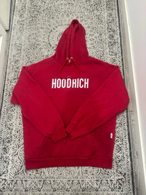 Röd hoodie från Hoodrich - Snygg röd hoodie från Hoodrich med vit logga broderad på bröstet. Klassisk huva med dragsko och ribbade muddar vid ärmar och nederkant. Tillverkad i mjukt bomullsmaterial som är skönt att bära. Perfekt för en avslappnad streetwear-look.