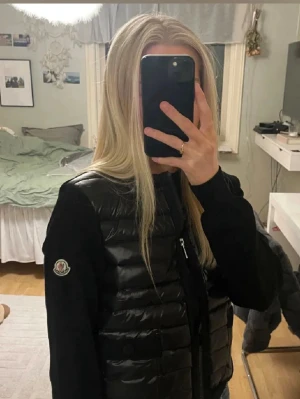 Svart cardiganjacka från Moncler - Snygg svart cardiganjacka från Moncler med quiltad framsida i glansigt material och stickade ärmar. Jackan har dragkedja, två fickor med knapp och ribbade muddar. Perfekt för lager-på-lager och streetstyle.