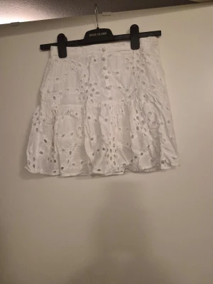 Vit volangkjol - Söt vit kortkjol med broderade hål och volangkant. Kjolen har en luftig och lätt känsla, perfekt för varma dagar. Den har ett romantiskt uttryck och passar till många olika stilar. Dragkedjan har gått av men det kan fortfarande att dra upp och ner.