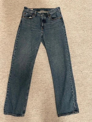 Levi's 501 blå jeans straight fit - Klassiska Levi's 501 jeans i blå denim med straight fit och femficksdesign. Jeansens material är bomull och de har en ikonisk läderpatch bak samt Levi's röda etikett på bakfickan. Perfekt för dig som gillar tidlös stil och enkelhet.