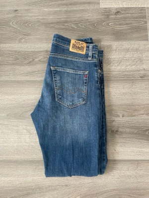 Blå jeans från Replay - Snygga blå jeans från Replay med raka ben och klassisk femficksmodell. Jeansen har en diskret tvättad look och detaljerade sömmar på bakfickorna. Tillverkade i slitstarkt denim med en bekväm passform. Perfekta för en avslappnad stil. Mycket bra skick! 