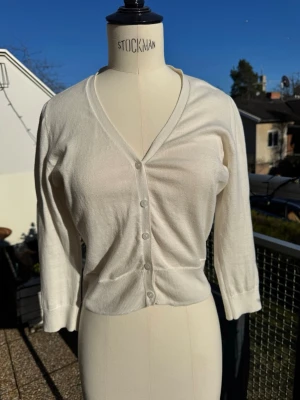 Vit kofta Ralph Lauren - Rarlph Lauren vit kofta med v-ringning och knäppning framtill. Modellen har trekvartsärmar och ribbade muddar vid ärmslut och nederkant. Smart att ha en kofta med sig på avslutningen om det blir kallt. 🌦️