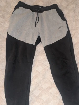 Nike tech mjukisbyxor - Snygga mjukisbyxor från Nike i svart och ljusgrått med dragsko i midjan och elastisk resår. Skriv vid intresse 