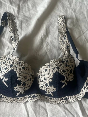 Mörkblå intimissmi bh - Elegant mörkblå bh från intimissmi med vacker vit spets och broderade blommor. Bh:n har vadderade kupor och breda axelband med spetsdetaljer. Perfekt för dig som gillar en feminin och lyxig stil. Använt typ 2 gånger för den va för stor