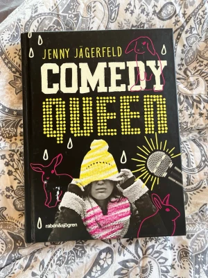Comedy Queen av Jenny Jägerfeld - En färgstark och modern roman med hård pärm, svart omslag med gula och vita detaljer samt illustrationer av djur och mikrofon. Boken är skriven av Jenny Jägerfeld och utgiven av Rabén & Sjögren. Perfekt för dig som gillar humor och starka berättelser.