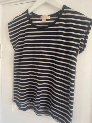Randig t-shirt från Michael Kors - Snygg blåvit randig t-shirt från Michael Kors med korta ärmar och rund halsringning. Perfekt till jeans eller kjol för en avslappnad men trendig look. Tillverkad i mjuk bomull som känns skön mot huden. unik och lyxig topp! Storlek S, lite oversize. 