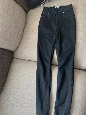 Svarta skinny jeans från lager 157 - Säljer ett par svarta skinny jeans från Gina Tricot med hög midja och klassisk femficksdesign. Jeansen har smal passform och silverfärgade nitar. Perfekta för dig som gillar en clean och enkel stil.