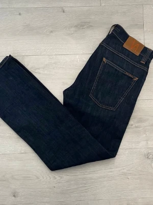 Mörkblåa nudie jeans - Säljer ett par stilrena mörkblå jeans från Nudie Jeans med regular fit. Klassisk modell som passar till allt och funkar både till vardag och mer uppstyrda outfits.  • Färg: Mörkblå • Fit: Regular fit • Skick: Bra skick • Bekväma och snygg passform • Enkel att matcha med hoodie, stickat eller t-shirt • Kvalitetsjeans med riktigt bra denimkänsla