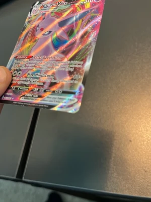 Pokémonkort Espeon VMAX - Säljer ett färgstarkt och glansigt Pokémonkort av Espeon VMAX med holografisk finish. Kortet har en mix av rosa, lila och regnbågsfärger och är tillverkat i tålig kartong. Perfekt för samlare eller dig som vill boosta din lek med en mäktig psychic-Pokémon.