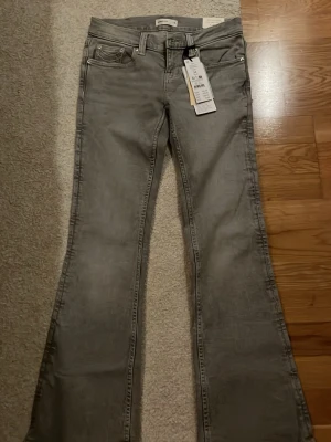 Grå bootcut jeans från Gina Tricot - Snygga grå lowwaist bootcut jeans från Gina Tricot med broderade sömmar på bakfickorna. Prislappen är kvar på, ej använda. Storlek 34 petite.