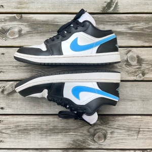 Nike Air Jordan 1 Low Black University Blue White - Nike Air Jordan 1 Low i svart, vitt och ljusblått skinn. Sparsamt använda så fortfarande i väldigt bra skick. Lite  creased  på framsidan men inte något man tänker på. Köpta i usa, New York, på fight club. Orginal boxen är inkluderad. 