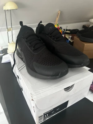 Nike Air Max 270 helsvarta sneakers - Säljer ett par helsvarta Nike Air Max 270 sneakers A kopior med mesh-överdel och synlig Air-enhet i hälen. Skorna har en sportig look med diskret Swoosh-logga på sidan och klassisk snörning. Perfekta för dig som gillar stilrena och bekväma sneakers.