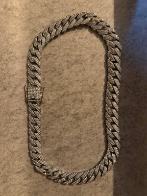 Cuban chain - Stilrent halsband i cuban chain-modell med silverfärg och tätt satta gnistrande stenar på framsidan. Halsbandet har en robust låsning och breda länkar som ger ett lyxigt och trendigt intryck. Perfekt för dig som vill sticka ut med accessoarer.