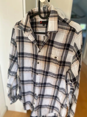 Rutig skjorta från Dressmann M - Snygg rutig skjorta från Dressmann i storlek M. Skjortan har ett klassiskt rutmönster i vitt, svart och beige med knappar framtill och en bröstficka. Perfekt för en avslappnad och stilren look.