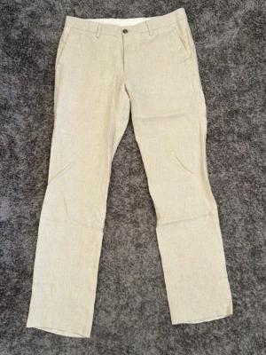 Beige linnebyxor med raka ben från dressman - Snygga beige linnebyxor med raka ben och klassisk passform. Byxorna har bälteshällor, sidofickor fram och två bakfickor med knapp. Perfekta för en avslappnad men stilren look. Tillverkade i svalt linnematerial. Storlek W30 L32