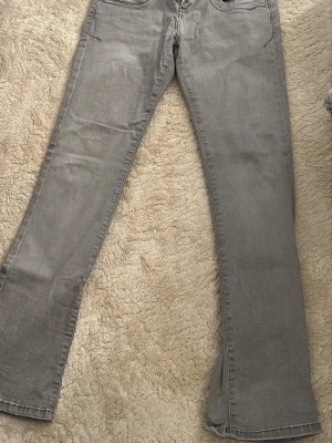 Grå bootcut jeans - Snygga grå jeans med bootcut passform och klassiska fem fickor. Jeansen har en stilren look och är perfekta för dig som gillar en avslappnad men trendig stil. Materialet är mjukt och stretchigt för extra komfort.
