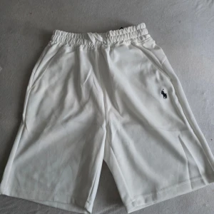 Vita shorts från Ralph Lauren - Snygga vita shorts från Ralph Lauren med elastisk midja och sidofickor. Klassisk logga broderad på ena benet. Perfekta för sommardagar och enkel att matcha med olika toppar.