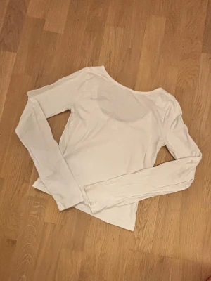 Vit långärmad topp med rund hals - En enkel och stilren vit långärmad topp med en rund typ open back  . Toppen är figurnära och passar perfekt till jeans eller kjol. Tillverkad i mjukt material som känns skönt mot huden.