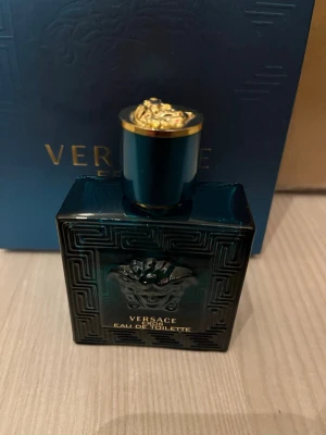 Versace Eros Eau de Toilette - Versace Eros Eau de Toilette i en lyxig mörkblå glasflaska med guldiga detaljer och Medusa-huvudet på framsidan. Flaskan har en fyrkantig form och elegant mönster. Perfekt för dig som gillar exklusiva dofter och snygg design.35-40ml,har liten spricka eller något på flaskan men är inte så farligt.