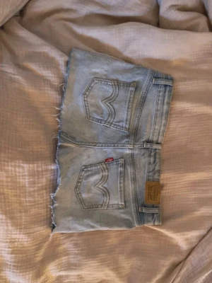 Ljusblå jeanskjol från Levi's - Ljusblå jeanskjol från Levi's!! Midjemåttet: ca 36, sitter som en xs men har stretch🥰perfekt till sommaren❣️har ett litet hål vi gylfen men inget jag tycker man märker av