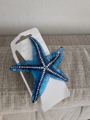 Blå sjöstjärneformad hårklämma - Helt ny, ej använd ✨️ Superfin hårklämma i form av en sjöstjärna i blått akrylmaterial med vita prickdetaljer. Perfekt för att ge en cool och unik touch till din frisyr. Klämman är lätt och smidig att använda och sticker verkligen ut med sin havsinspirerade design.