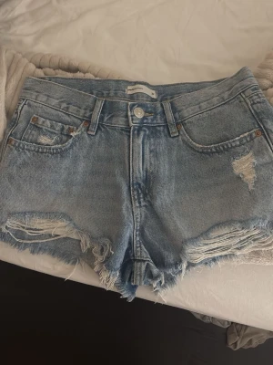 Ljusblå denimshorts från perfect jeans - Snygga ljusblå denimshorts från Perfect Jeans med fransig kant och slitna detaljer. Klassisk femficksmodell med knapp och dragkedja framtill. Perfekta för varma dagar och en avslappnad stil. Säljer för att de är för små för mig.💕💕