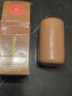 Rhode Pocket Blush Tan Line - Rhode Pocket Blush i färgen Tan Line är ett krämrouge i stickformat. Färgen är en varm, brunrosa nyans som ger en naturlig glow. Enkel att applicera direkt på kinderna och perfekt att ha med i väskan. Snygg, kompakt förpackning i beige plast med Rhode-logga.