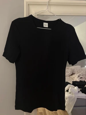 Svart basic t-shirt  - En svart vanlig lite figyrsydd tshirt från Gina. Knappt använd. Säljer för 40kr + frakt