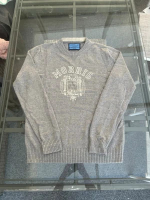 Morris Knit Sweater Grey – Clean Preppy Old Money Fit - Säljer en sjukt clean Morris knit sweater i grå färg, storlek M. Klassisk stickad tröja i 100% cotton med stor Morris-logo framtill som ger en riktig old money / preppy aesthetic. Perfekt för dig som gillar clean fit, quiet luxury och minimalist Scandinavian style.  Tröjan har en snygg regular fit och funkar perfekt till jeans, chinos eller över en skjorta för en mer business casual look. Mjuk och bekväm knitted sweater som passar året runt och är enkel att styla i både casual och streetwear.