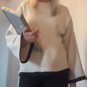 Beige oversized stickad tröja - Snygg beige stickad tröja med vida ärmar och svarta detaljer längs ärmslut och nederkant. Oversized passform som ger en avslappnad look. Perfekt att matcha med jeans eller leggings.