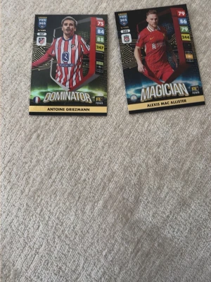 FIFA 365 fotbollssamlarkort - Två FIFA 365 samlarkort från Panini med spelarna Antoine Griezmann och Alexis Mac Allister. Kortet med Griezmann har rödvitrandig tröja och texten 'Dominator', medan Mac Allister har röd tröja och texten 'Magician'. Perfekt för samlare av fotbollskort.