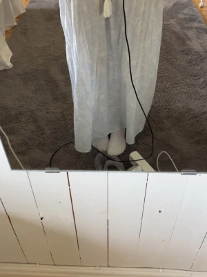Ljusblå långkjol från Gina Tricot - Ljusblå långkjol från Gina Tricot med diskret blommigt mönster och smock i midjan. Kjolen har en avslappnad passform och dekorativ knytning med tofs framtill. Perfekt för en somrig look.