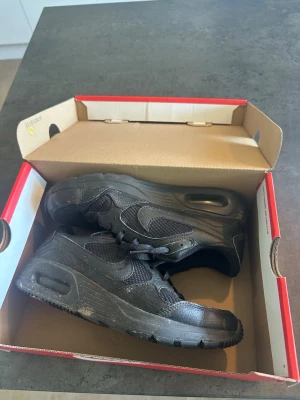 Svarta Nike Air Max sneakers - Säljer ett par helsvarta Nike Air Max sneakers med klassisk luftsula och meshpaneler för extra andningsförmåga. Skorna har en sportig look med diskreta detaljer och är perfekta för dig som gillar streetwear och komfort. Snygg design med Nike-logga på sidan.