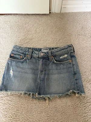 Blå jeanskjol från Weekday - Säljer en kort blå jeanskjol från Weekday med slitna detaljer och fransig nederkant. Använd fåtal gånger💕 Säljer då den tyvärr blivit för liten💕