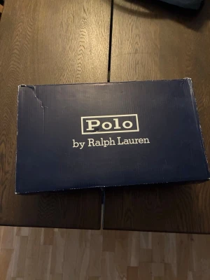Vita sneakers från Polo Ralph Lauren - Stilrena vita sneakers från Polo Ralph Lauren med klassisk låg profil och vita snören. Skorna är tillverkade i slätt läder och har en enkel, clean design som passar till det mesta. Perfekta för dig som gillar minimalistisk och tidlös stil. Skorna är oanvända