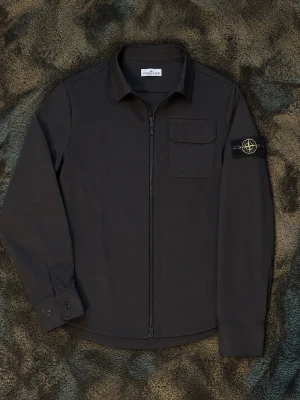 Stone island overshirt  - Snygg svart overshirt från Stone Island med dragkedja och logga på vänster ärm. Overshirten har en bröstficka och är tillverkad i ett lätt, slitstarkt material som ger en clean och modern look. Perfekt att bära över en t-shirt för en avslappnad stil. Utan att överdriva så kan detta vara den skönaste overshirten/vind jackan eftersom att den har både mjukt material och puttar bort vinden så att vinden inte går rakt igenom jackan. Jackan är helt autentisk och har original lapparna. Skriv vid frågor