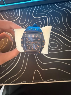 Blå snygg klocka - Stilren klocka med blått armband och rektangulärt ur i blått och guld. Urtavlan har flera små ur och tydliga indexmarkeringar. Armbandet är i syntetmaterial och spännet är i metall. Perfekt accessoar för dig som vill sticka ut.👍🏼 PRISET ÄR INTE HUGGET I STEN!