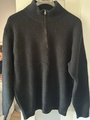 Svart stickad tröja med halv dragkedja - Säljer en svart stickad tröja från Uniqlo i storlek M. Tröjan har hög krage och halv dragkedja framtill, vilket ger en sportig och stilren look. 