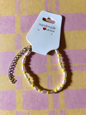 Handgjort pärlarmband i gult och vitt - Säljer ett handgjort armband med vita och gula pärlor. Armbandet har en tunn kedja i silverfärg för justerbar storlek och är perfekt för att ge en färgklick till din outfit. Enkel och söt design som passar dig som gillar unika accessoarer.