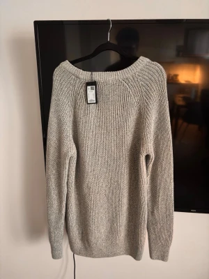 Ljusgrå stickad tröja H&M - En stilren ljusgrå stickad tröja med rund halsringning och långa ärmar. Tröjan har en klassisk rak passform och är tillverkad i ett mjukt, grovstickat material som passar perfekt för kyligare dagar.