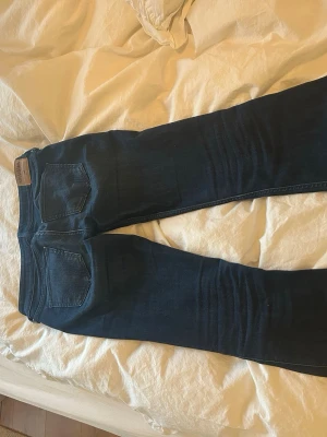 Mörkblå bootcut jeans med slitningar - Snygga mörkblå bootcut jeans från Hollister med slitna detaljer på knäna och klassiska bakfickor. Jeansen har en låg midja och är tillverkade i denim med lite stretch för skön passform. Perfekta för en avslappnad och trendig look.